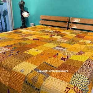 Könnte beinhalten: Ein Patchwork-Quilt in Gelb- und Goldtönen bedeckt ein Bett. Der Quilt besteht aus verschiedenen Stoffquadraten mit unterschiedlichen Mustern und Texturen. Das Bett hat ein hölzernes Kopfteil. Das Bild enthält den Text "copyright of thejaipurcart".