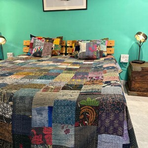 Puede incluir: Una colcha de retazos con una variedad de colores y patrones, incluyendo dise&ntilde;os florales, geom&eacute;tricos y paisley. La colcha est&aacute; hecha de telas recicladas y est&aacute; cosida a mano. Est&aacute; colocada sobre una cama con almohadas y una cabecera de madera.