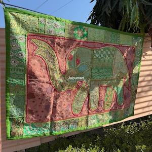 May include: A rectangular textile wall hanging featuring an embroidered elephant design. The elephant is green with intricate patterns, set against a pinkish-brown background. The border is green with red accents and the text "Jaipurcart".