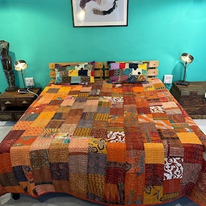 Könnte beinhalten: Ein Patchwork-Quilt in Orange-, Rot- und Brauntönen bedeckt ein Bett. Der Quilt besteht aus verschiedenen Stoffquadraten. Zwei dekorative Kissen mit Patchwork-Designs liegen auf dem Bett. Ein hölzernes Kopfteil und Nachttische flankieren das Bett.