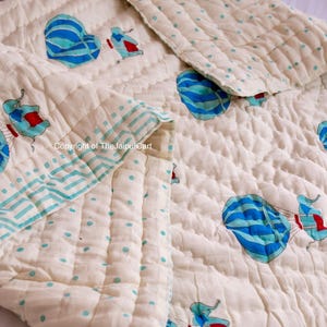 K&ouml;nnte beinhalten: Eine wei&szlig;e Babydecke aus Baumwolle mit einem Muster aus blauen und wei&szlig;en Hei&szlig;luftballons und roten und wei&szlig;en Elefanten. Die Decke hat einen hellblauen und wei&szlig;en Punkt-Rand.