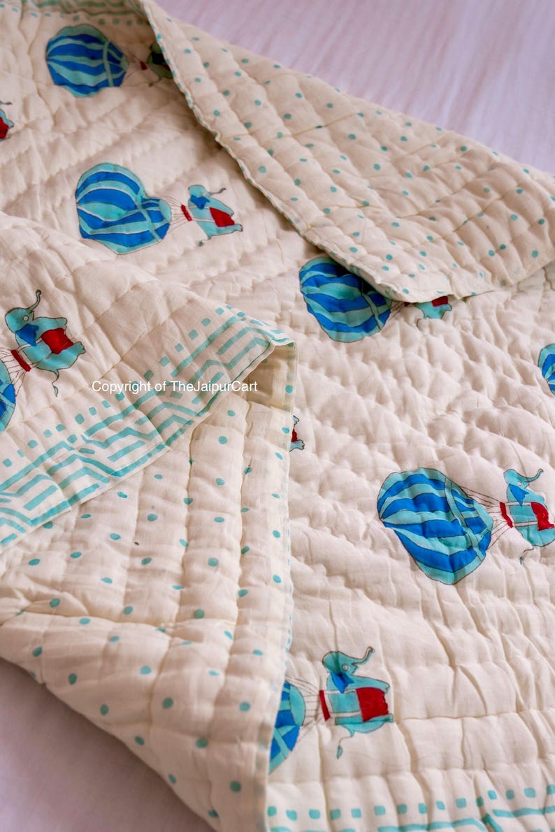 K&ouml;nnte beinhalten: Eine wei&szlig;e Babydecke aus Baumwolle mit einem Muster aus blauen und wei&szlig;en Hei&szlig;luftballons und roten und wei&szlig;en Elefanten. Die Decke hat einen hellblauen und wei&szlig;en Punkt-Rand.