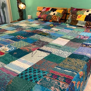 Puede incluir: Una colcha de retazos hecha de recortes de tela coloridos en tonos azules, verdes y morados. La colcha est&aacute; extendida sobre una cama con dos fundas de almohada a juego.