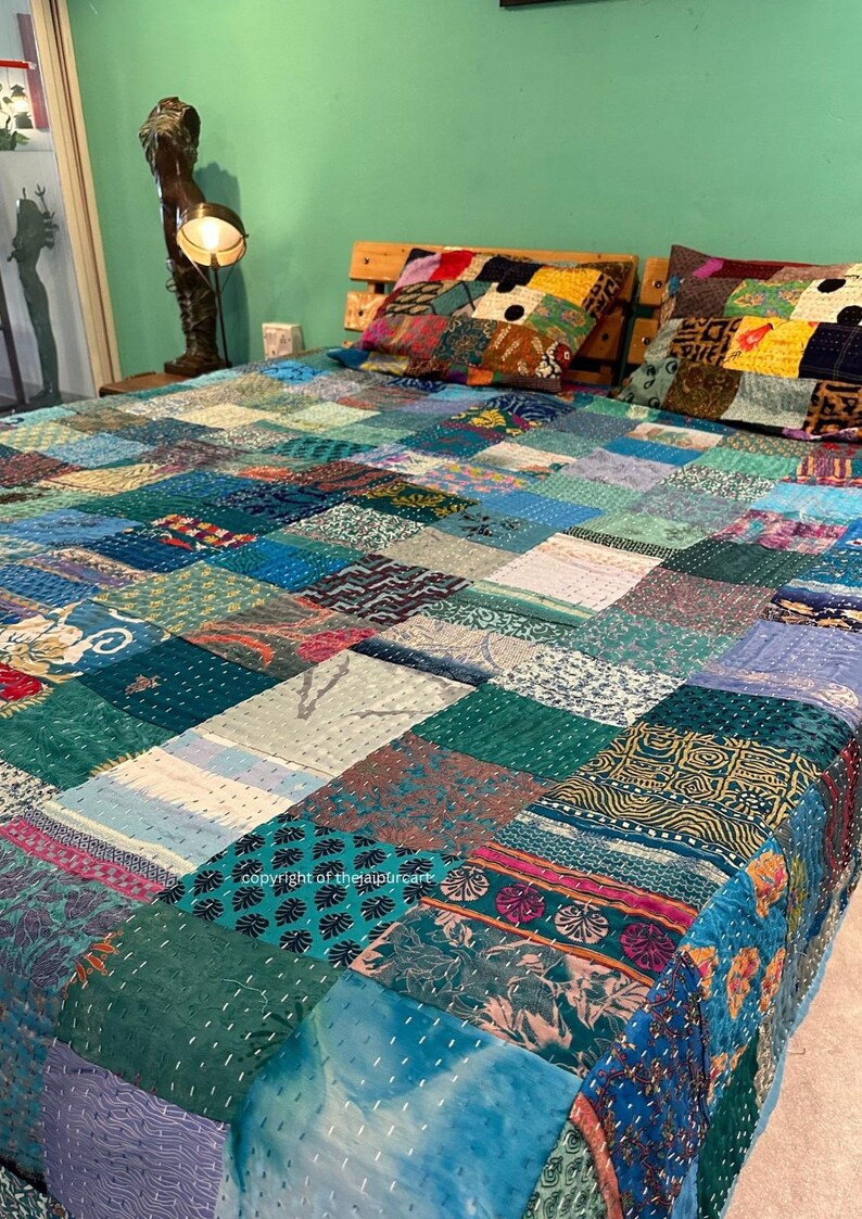 Puede incluir: Una colcha de retazos hecha de recortes de tela coloridos en tonos azules, verdes y morados. La colcha est&aacute; extendida sobre una cama con dos fundas de almohada a juego.