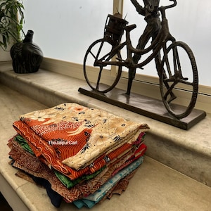 May include: A stack of colorful fabric scraps with floral and geometric patterns. The fabric is folded neatly and arranged on a marble surface. The text "TheJaipurCart" is visible on the fabric.