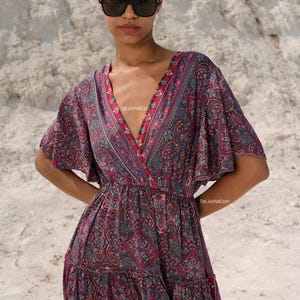 K&ouml;nnte beinhalten: Ein Paisley-Kleid in Burgunder-, Lila- und T&uuml;rkist&ouml;nen. Das Kleid hat einen V-Ausschnitt, kurze &Auml;rmel und einen Stufenrock. Der Text "THEJAIPURCART" ist sichtbar. Die Person tr&auml;gt eine Sonnenbrille.
