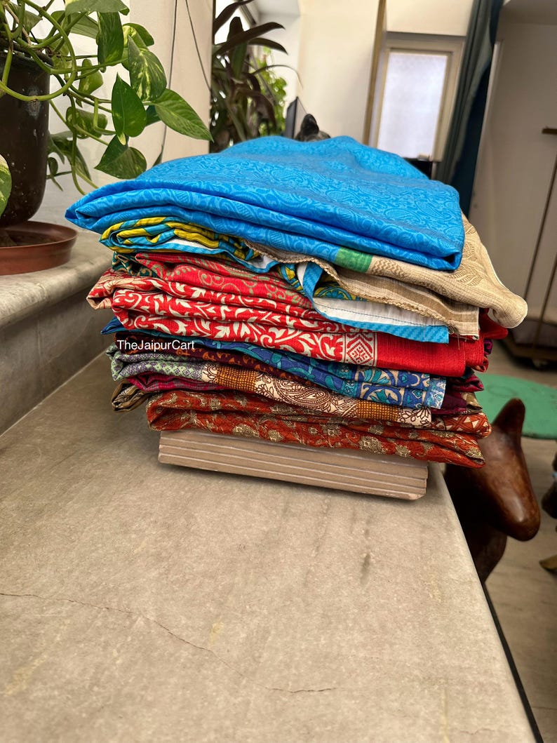 May include: A stack of colorful fabric scraps with various patterns and textures. The fabric scraps are folded neatly and arranged on a light brown surface. The text "TheJaipurCart" is visible on the fabric.