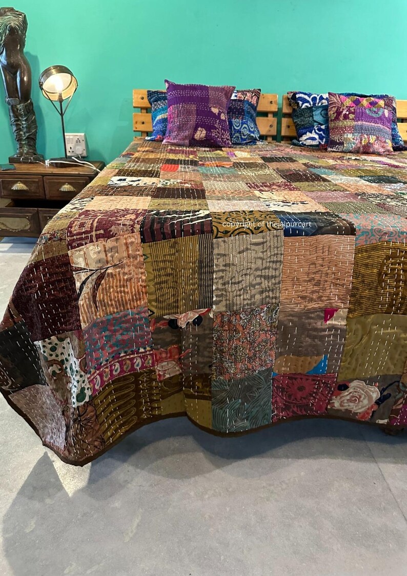 Puede incluir: Una colcha de retazos hecha de una variedad de telas en tonos marrones, beige y morados. La colcha est&aacute; colocada sobre una cama con dos almohadas decorativas.