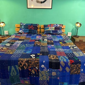Puede incluir: Un edred&oacute;n azul de patchwork con una variedad de patrones coloridos. El edred&oacute;n est&aacute; colocado sobre una cama con dos fundas de almohada a juego. La cama est&aacute; en una habitaci&oacute;n con paredes de color turquesa y dos l&aacute;mparas sobre mesitas de noche.