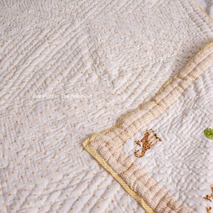 K&ouml;nnte beinhalten: Wei&szlig;e und gelbe Babydecke mit einem kleinen Giraffenmuster. Die Decke ist mit einem Rautenmuster gesteppt und hat einen gelben Rand.