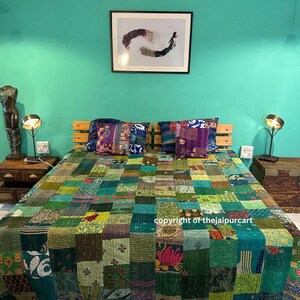 Puede incluir: Una colcha de patchwork verde con una variedad de colores y patrones. La colcha está sobre una cama con dos almohadas y dos lámparas sobre mesitas de noche. La pared detrás de la cama es de un color verde azulado brillante.