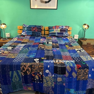May include: A patchwork quilt in shades of blue, with squares of various patterns and textures. Two matching pillowcases rest on a wooden headboard. The quilt is on a bed in a room with a green wall and artwork.