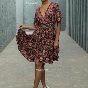 K&ouml;nnte beinhalten: Ein kurzes, schwarzes Kleid mit rotem Paisley-Muster. Das Kleid hat einen V-Ausschnitt und kurze &Auml;rmel. Das Model tr&auml;gt wei&szlig;e Turnschuhe. Der Text "The Jaipur Cart" ist sichtbar.