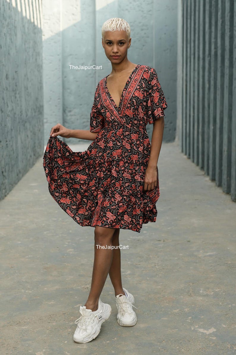 K&ouml;nnte beinhalten: Ein kurzes, schwarzes Kleid mit rotem Paisley-Muster. Das Kleid hat einen V-Ausschnitt und kurze &Auml;rmel. Das Model tr&auml;gt wei&szlig;e Turnschuhe. Der Text "The Jaipur Cart" ist sichtbar.