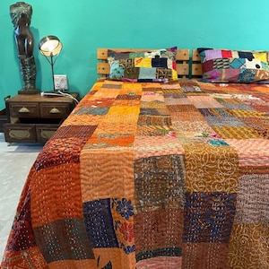 Puede incluir: Una colcha de retazos con una variedad de colores y patrones, incluyendo naranja, marrón, azul y verde. La colcha está hecha de diferentes telas y está acolchada con una puntada corrida. La colcha está en una cama con dos almohadas.