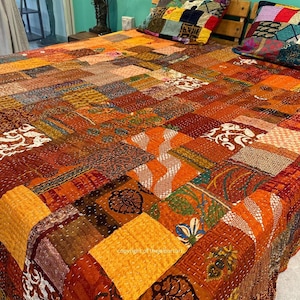 Peut inclure: Une courtepointe patchwork avec une variété de couleurs et de motifs, notamment orange, marron, jaune et blanc. La courtepointe est faite de nombreux tissus différents cousus ensemble dans un motif aléatoire. La courtepointe est sur un lit avec deux oreillers.