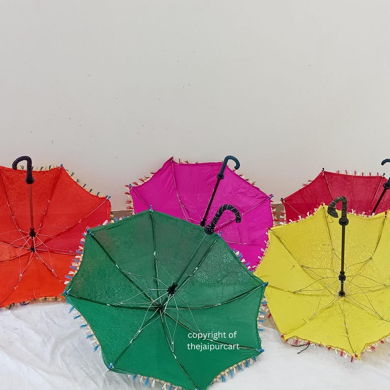 Puede incluir: Cinco paraguas coloridos con ribete de flecos y mangos negros. Los paraguas son rojo, rosa, verde, amarillo y azul.