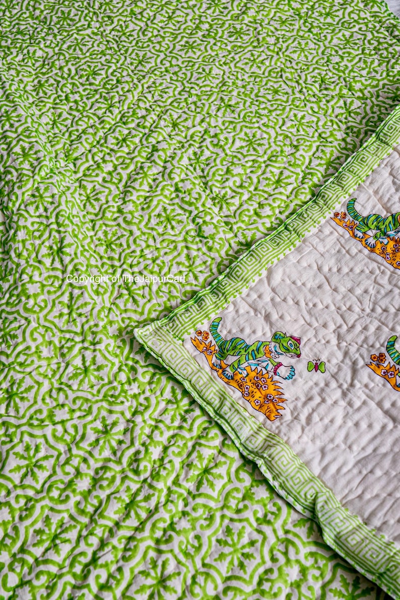 K&ouml;nnte beinhalten: Eine gr&uuml;ne und wei&szlig;e Baumwolldecke mit einem sich wiederholenden geometrischen Muster. Die Decke hat einen Rand mit einem sich wiederholenden griechischen Schl&uuml;sselmuster. Die andere Seite der Decke hat einen wei&szlig;en Hintergrund mit einem gr&uuml;nen Rand und einem sich wiederholenden Muster von Tigern.