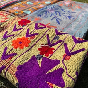 Peut inclure: Gros plan sur plusieurs textiles brodés colorés. Le premier plan présente un textile jaune avec de grands motifs floraux violets et des accents de fleurs orange et rouges. D'autres textiles en arrière-plan ont des motifs bleus, orange et roses.