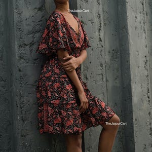 K&ouml;nnte beinhalten: Schwarzes und rotes Kleid mit Paisley-Muster, V-Ausschnitt und kurzen &Auml;rmeln. Das Kleid hat einen Stufenrock und wird mit wei&szlig;en Turnschuhen getragen. Der Text "TheJaipurCart" ist im Bild sichtbar.