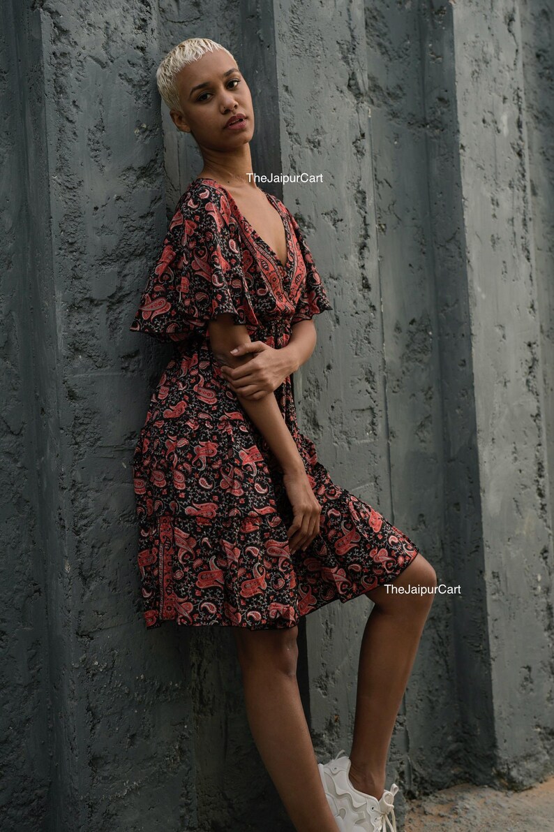 K&ouml;nnte beinhalten: Schwarzes und rotes Kleid mit Paisley-Muster, V-Ausschnitt und kurzen &Auml;rmeln. Das Kleid hat einen Stufenrock und wird mit wei&szlig;en Turnschuhen getragen. Der Text "TheJaipurCart" ist im Bild sichtbar.