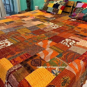 Può includere: Un trapunta patchwork con una varietà di colori e motivi, tra cui arancione, marrone e verde. La trapunta è realizzata con diversi tessuti cuciti insieme in un motivo casuale. La trapunta è su un letto con due cuscini.