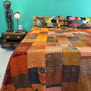 Puede incluir: Una colcha de retazos con una variedad de colores y patrones, incluyendo naranja, marr&oacute;n, azul y verde. La colcha est&aacute; hecha de diferentes telas y est&aacute; acolchada con una puntada corrida. La colcha est&aacute; en una cama con dos almohadas.