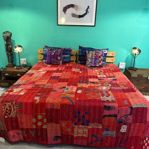 Puede incluir: Un edred&oacute;n rojo de patchwork con una variedad de patrones y colores, incluyendo rosa, azul y dorado. El edred&oacute;n est&aacute; colocado sobre una cama con dos almohadas y una cabecera de madera. La habitaci&oacute;n est&aacute; pintada de un color turquesa brillante.