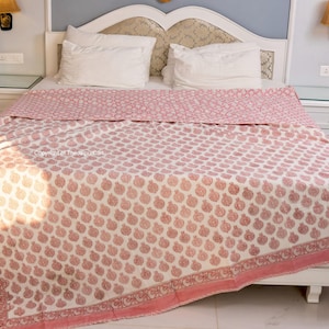 May include: A white cotton quilt with a pink floral pattern. The quilt is folded on a bed with white pillowcases.