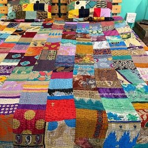 Könnte beinhalten: Eine farbenfrohe Patchwork-Decke aus wiederverwendeten Saris. Die Decke besteht aus Quadraten in verschiedenen Farben und Mustern, darunter florale, Paisley- und geometrische Designs. Die Decke ist ein lebendiges und vielseitiges Stück Wohnkultur.