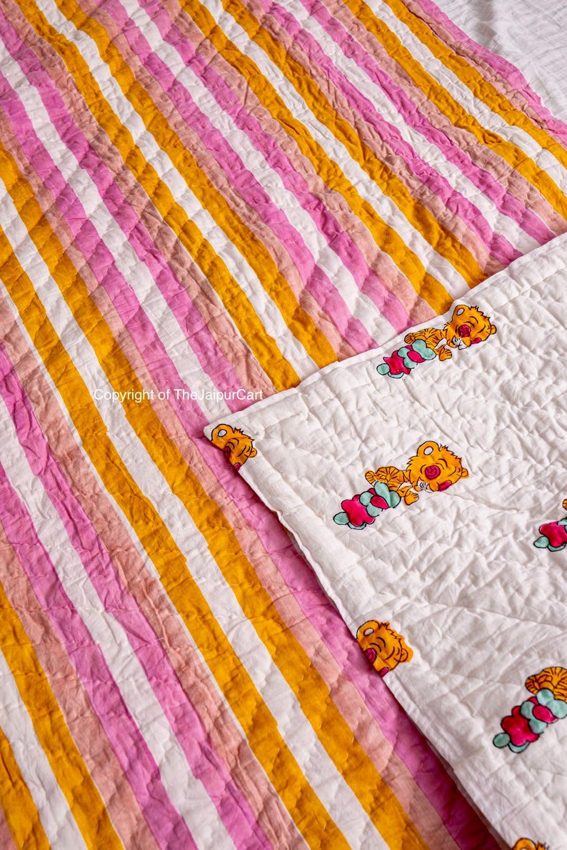 K&ouml;nnte beinhalten: Eine wei&szlig;e und rosafarbene gestreifte Steppdecke mit einem gelben Streifen. Die Steppdecke ist in der Mitte gefaltet und zeigt eine wei&szlig;e Seite mit einem Muster aus Comic-Tigern. Der Text "Copyright of TheJaipurCart" ist auf der Steppdecke sichtbar.