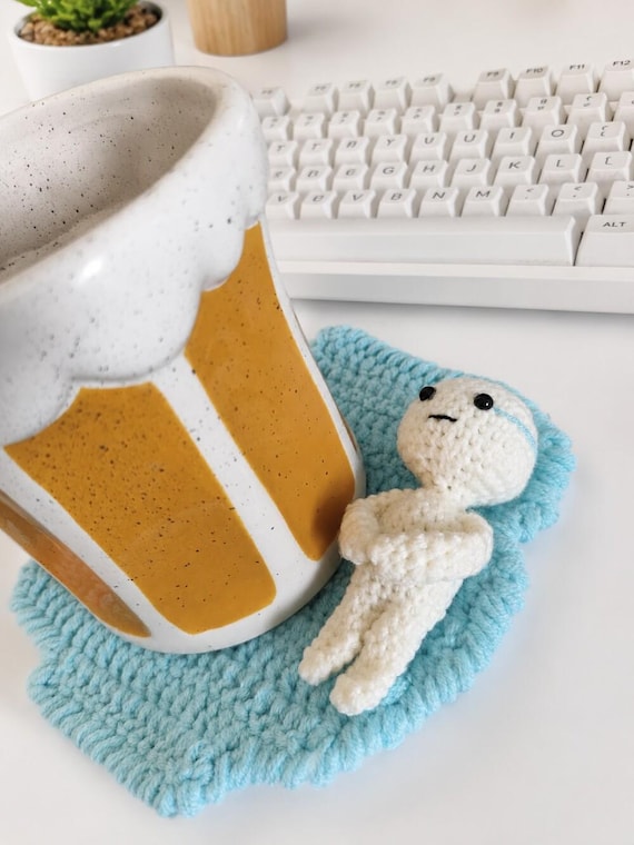 A hand-crocheted coaster shaped like the exhausted lying-down crying boy meme — absurdly specific and genuinely skilled craft.