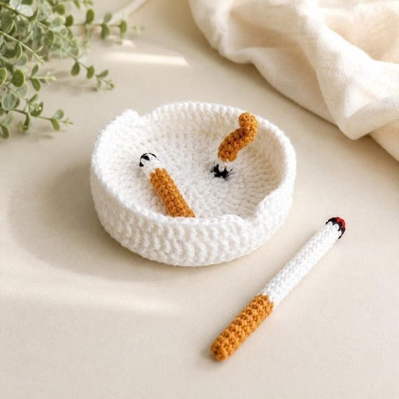 A crocheted ashtray complete with yarn cigarettes — a fully absurd, 100% handmade desk object that is simultaneously coaster, art piece, and conversation starter.