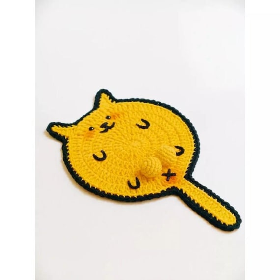 A chonky crochet cat clutching a tiny 3D ball as your coaster — absurdly cute, genuinely handmade, and does an actual job on your desk.