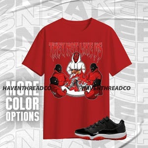Camiseta unisex AJ 11 Low Bred &quot;They Not Like Us&quot; en rojo, negro y blanco. Sudadera con capucha y zapatillas a juego. Camisa de lona Bella.