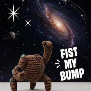 Puede incluir: Una criatura de ganchillo marrón con un brazo levantado, detalles turquesa y cuatro patas se encuentra frente a un fondo de galaxia. El texto "FIST MY BUMP" se muestra en blanco. La imagen tiene un tema espacial.