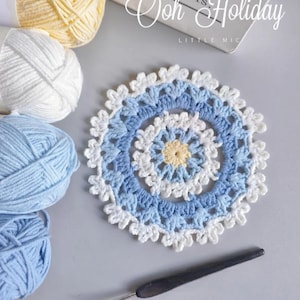 May include: A handmade crochet coaster with a floral design in shades of blue, white, and yellow. The coaster is surrounded by balls of yarn in matching colors, a crochet hook, and the text "Ooh Holiday" and "Good Photos, Good Design".