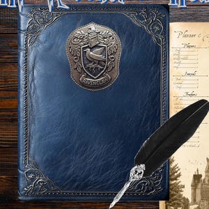 May include: A blue leather-bound planner with the text "HP Ravenclaw House Planner" in a stylized font. The planner features a Ravenclaw crest and an open page with a printed agenda and a quill pen.