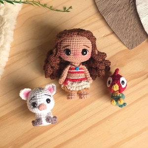 Puede incluir: Una muñeca de ganchillo con largo cabello castaño, tez bronceada y un conjunto de estampado rojo y blanco, acompañada de una pequeña figura de cerdo blanco con orejas rosas y un diminuto pájaro rojo, amarillo y verde. Texto BOSQUEGURUMI.