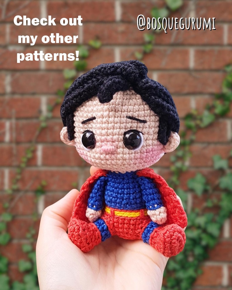 May include: A handmade crochet Superman doll with a red cape, blue and red suit, and black hair. The doll is sitting and has large black eyes. Text on the image reads "Check out my other patterns!" and "@BOSQUEGURUMI".