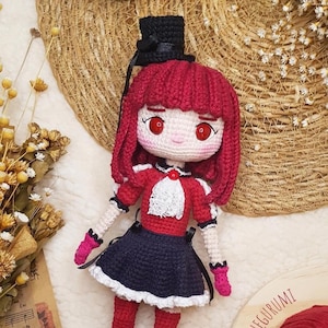 May include: A handcrafted crochet doll with red hair and a black top hat. The doll is dressed in a red and white outfit with a navy blue skirt. The doll has red eyes and pink gloves. A unique, handmade item.