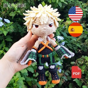 May include: A handmade crochet doll of a character with spiky blonde hair, red eyes, and a determined expression. The doll wears a black and green outfit with orange accents. The text "BOSQUEGURUMI" and "@bosquegurumi" are visible.