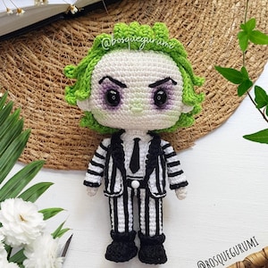 Könnte beinhalten: Handgefertigte Häkelpuppe einer Figur mit grünen Haaren, weißem Gesicht und einem schwarz-weiß gestreiften Anzug. Die Puppe hat einen strengen Ausdruck mit dunklen Augen und Augenbrauen. Die Puppe ist etwa 15 cm groß. Ein einzigartiges, handgefertigtes Produkt.