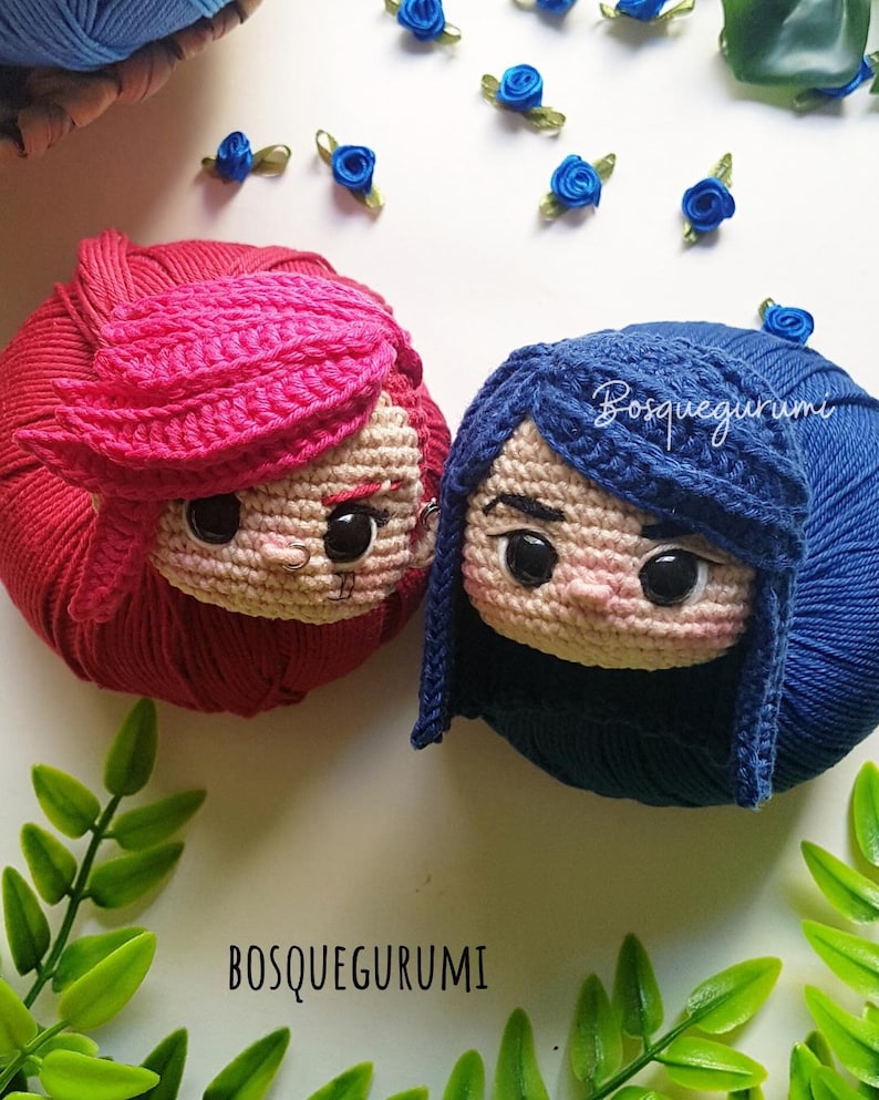 Pode incluir: Duas bonecas de croch&ecirc; com cabelo de l&atilde;, uma com l&atilde; vermelha e a outra com l&atilde; azul. As bonecas t&ecirc;m olhos grandes e est&atilde;o sentadas em uma superf&iacute;cie branca. O texto "BOSQUEGURUMI" &eacute; vis&iacute;vel na imagem.