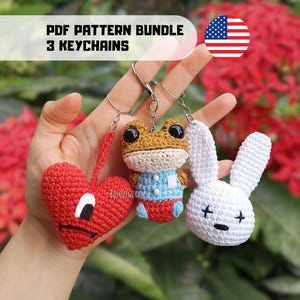 May include: Three handmade crochet keyrings: a red heart with a face, a frog in a blue shirt, and a white bunny. The keyrings are crafted with detailed stitching. The text "PDF PATTERN BUNDLE 3 KEYCHAINS" is displayed above the keyrings.
