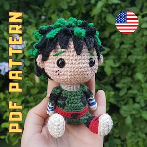 May include: Crocheted amigurumi doll with green hair, a green and black shirt, and red and white shoes. The doll is sitting on a hand.