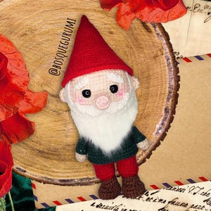 May include: A handmade crochet gnome doll with a red pointed hat, white beard, and rosy cheeks. The gnome wears a green sweater, red pants, and brown boots. The text "@BOSQUEGURUMI" is visible on the left side of the image.