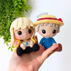 May include: Two crocheted dolls, one with blonde hair and a necklace, the other with gray hair and a yellow hat. The dolls are handmade with black eyes and rosy cheeks. The text "BOSQUEGURUMI" is visible.