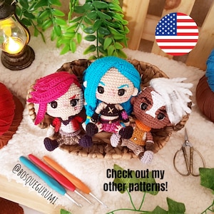 Pode incluir: Tr&ecirc;s bonecas amigurumi de croch&ecirc; em uma cesta de vime. As bonecas est&atilde;o vestidas com roupas diferentes e t&ecirc;m cores de cabelo diferentes. As bonecas est&atilde;o sentadas em uma cesta de vime. H&aacute; agulhas de croch&ecirc; e fio em primeiro plano. O texto "Check out my other patterns!" est&aacute; escrito na imagem.