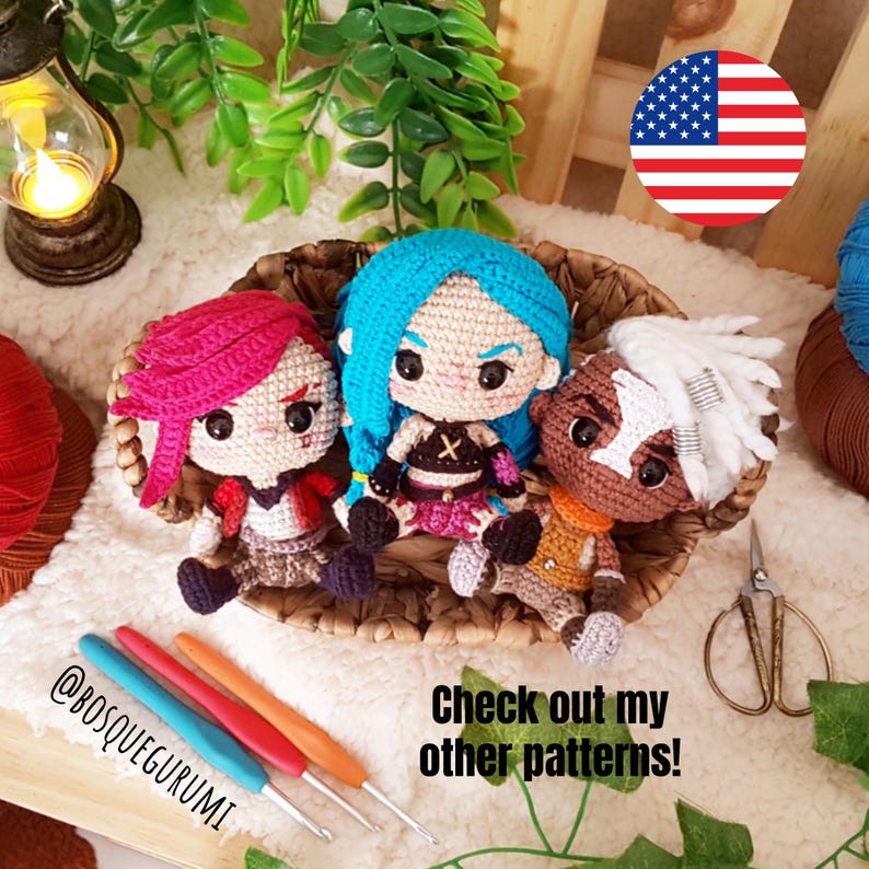 Pode incluir: Tr&ecirc;s bonecas amigurumi de croch&ecirc; em uma cesta de vime. As bonecas est&atilde;o vestidas com roupas diferentes e t&ecirc;m cores de cabelo diferentes. As bonecas est&atilde;o sentadas em uma cesta de vime. H&aacute; agulhas de croch&ecirc; e fio em primeiro plano. O texto "Check out my other patterns!" est&aacute; escrito na imagem.